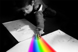 Black background with boy creating a rainbow on white paper with his fingers
